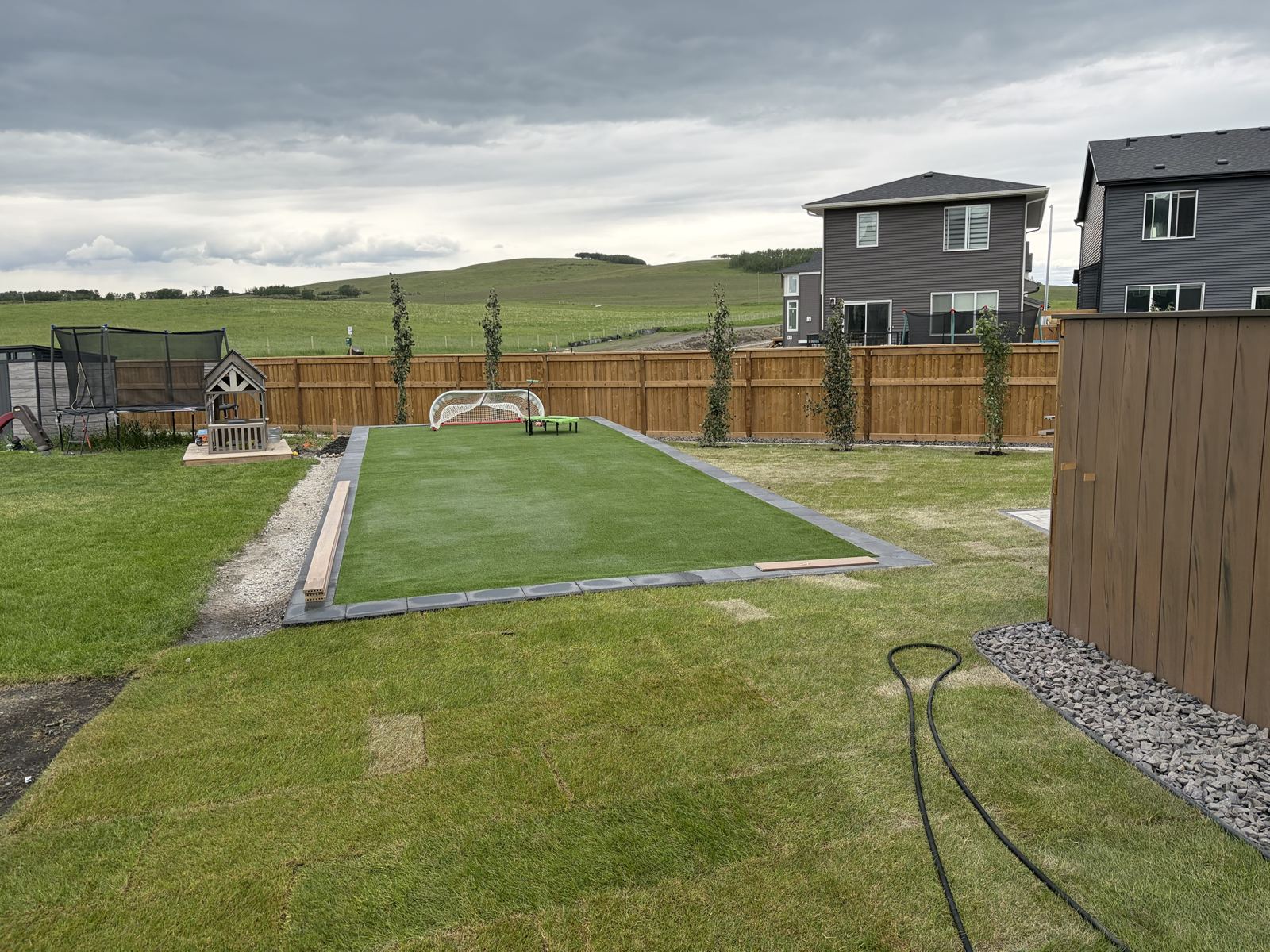 Completed backyard with artificial turf, block border, cedar fence and new trees