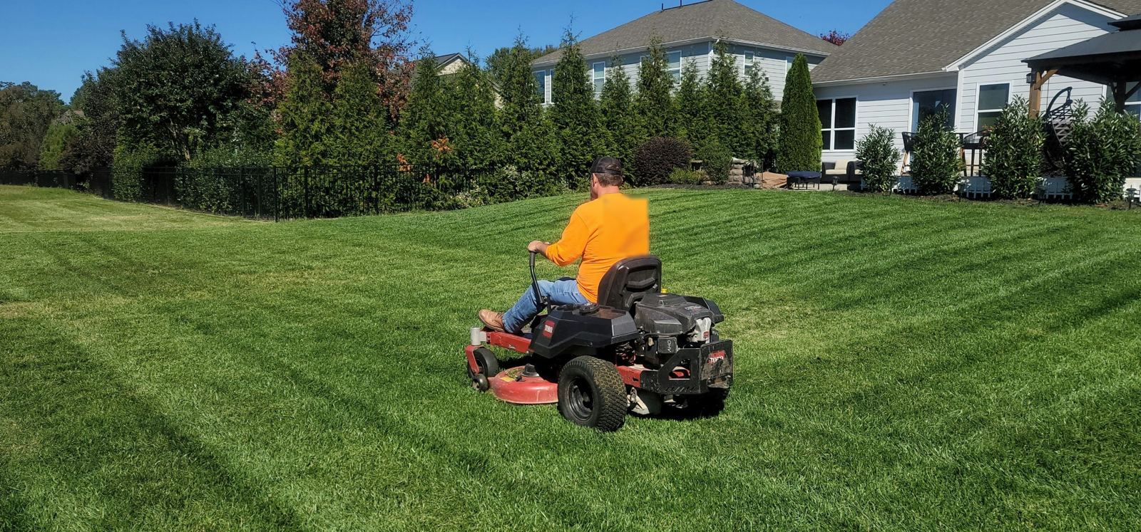 Ride-on mower cutting stripes in a large green lawn